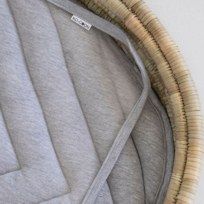 Gray quilted pad inside a wicker basket on a light background
