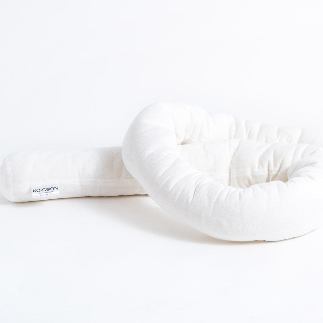 A white wool noodle pillow designed to be used as a cot bumper or a border for a baby's sleeping pod.