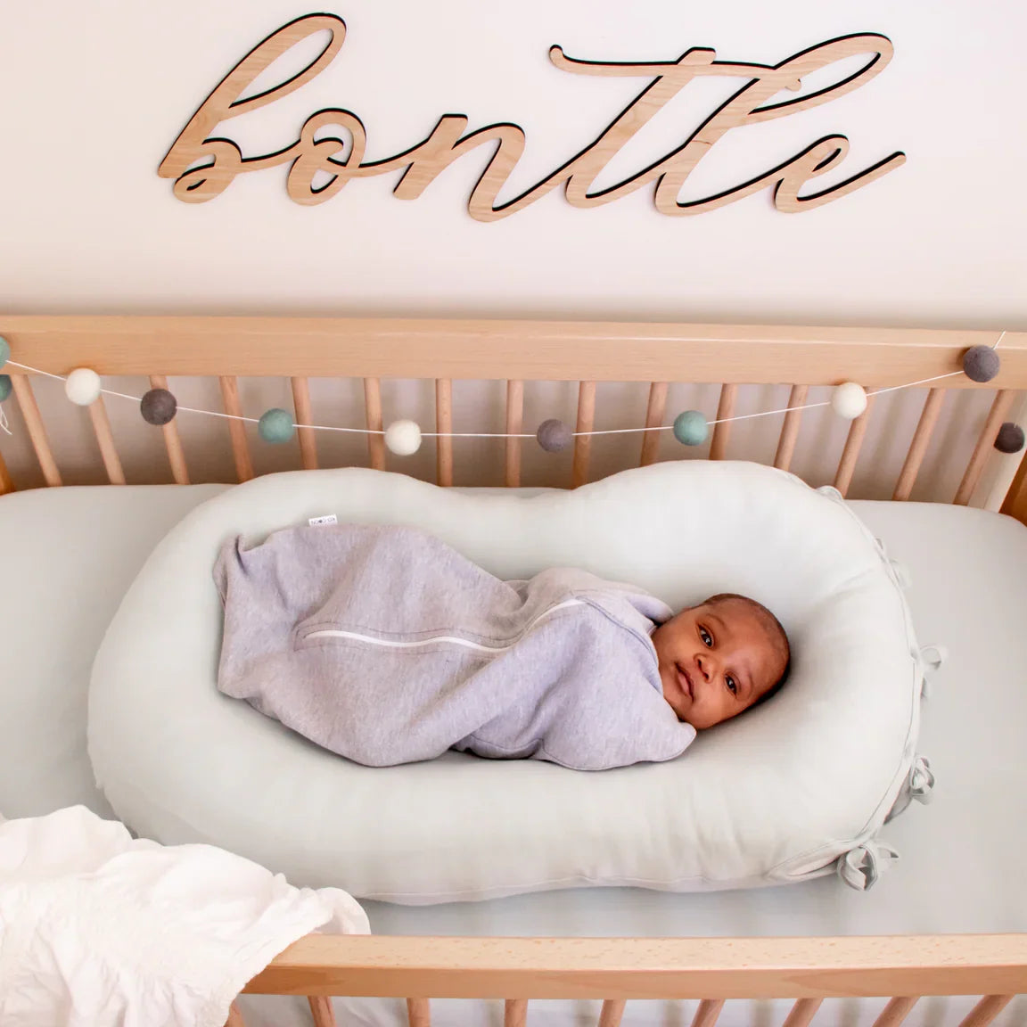 Newborn asleep in a Merino Nesting Pod with the white newborn cover inside a cot