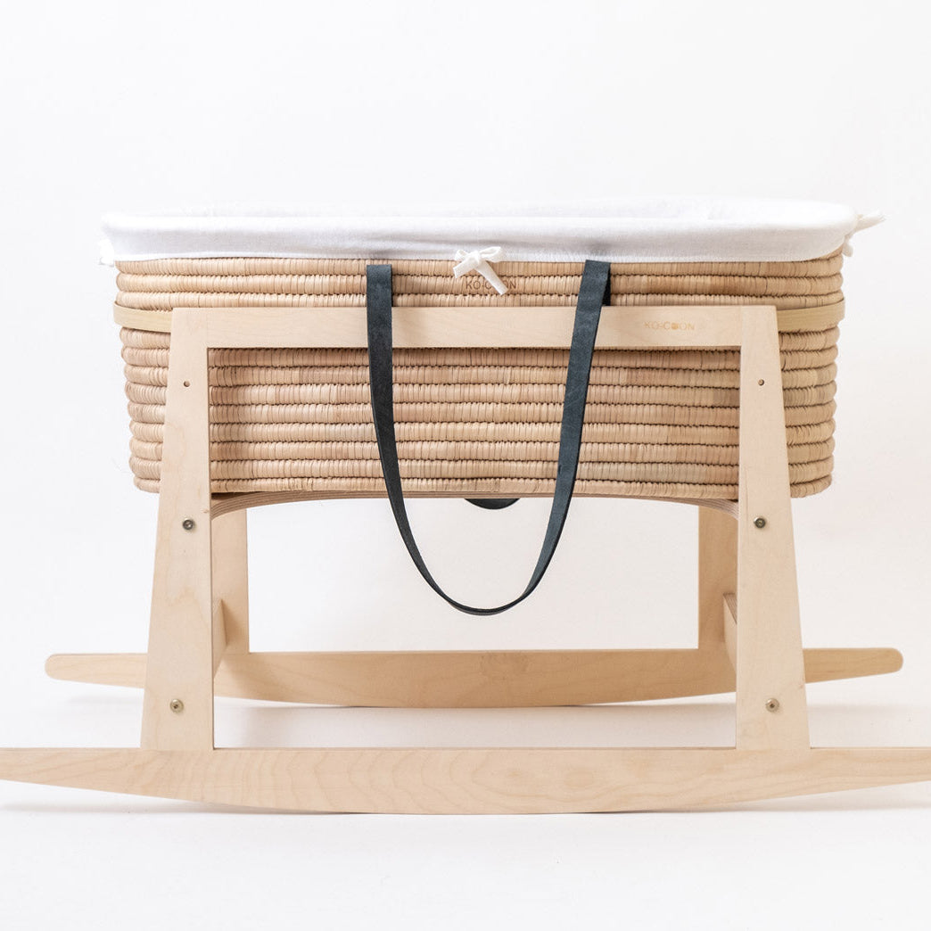 A Moses basket with black leather handles and white liner on a rocking stand.