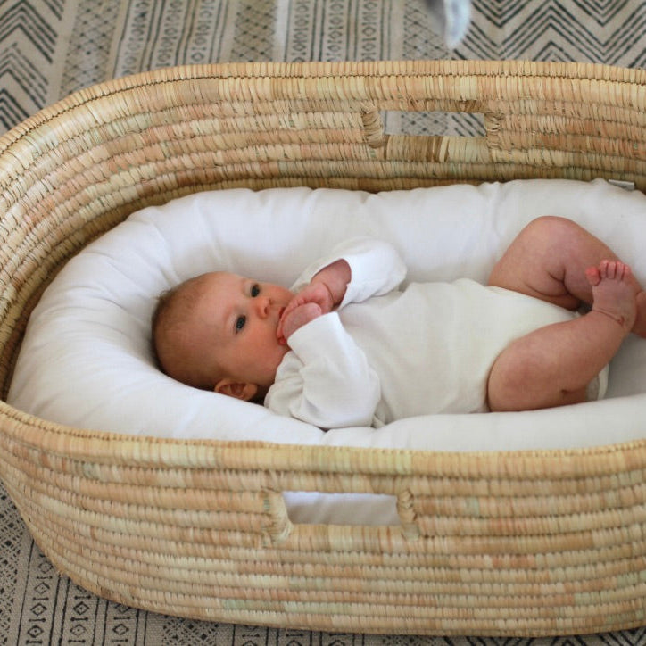 Baby lying in a KO-COON Milky White nesting pod inside a woven Moses basket