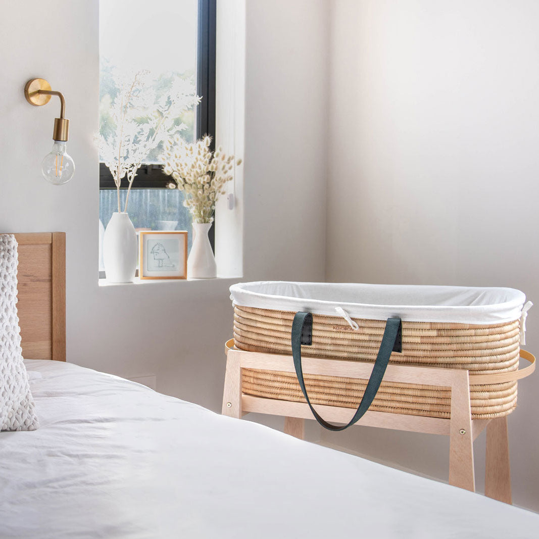 Moses basket with white liner next to a bed in a bedroom setting